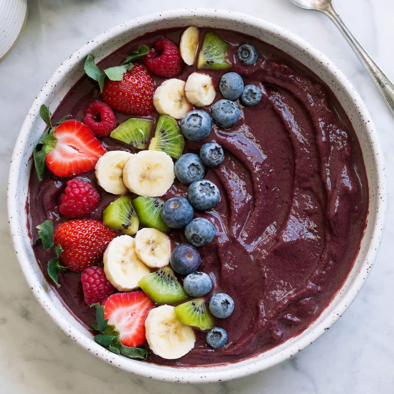 A bowl of acai smoothie with berries on a marble surface
